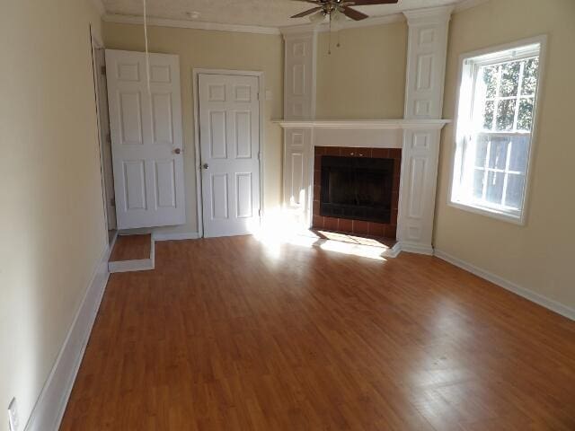 unfurnished living room featuring ceiling fan, ornamental molding, dark hardwood / wood-style floors, and a tiled fireplace