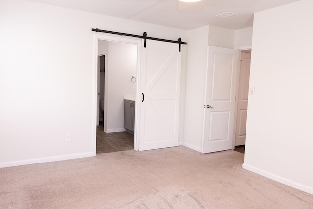 unfurnished bedroom featuring carpet, baseboards, a barn door, and connected bathroom