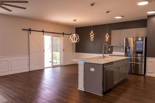 kitchen featuring stainless steel appliances, a sink, a decorative wall, a barn door, and a wainscoted wall