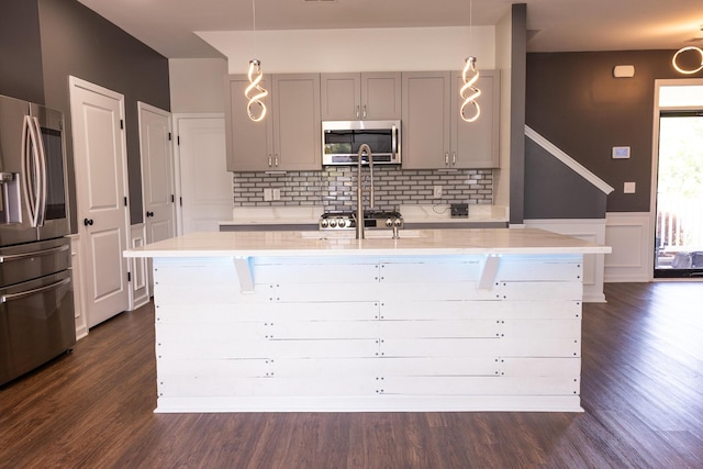kitchen featuring appliances with stainless steel finishes, gray cabinetry, decorative backsplash, an island with sink, and dark wood-type flooring