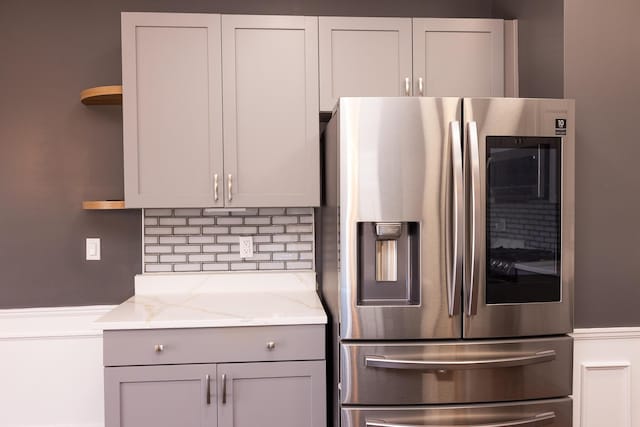 kitchen with stainless steel fridge with ice dispenser, open shelves, tasteful backsplash, and light stone counters