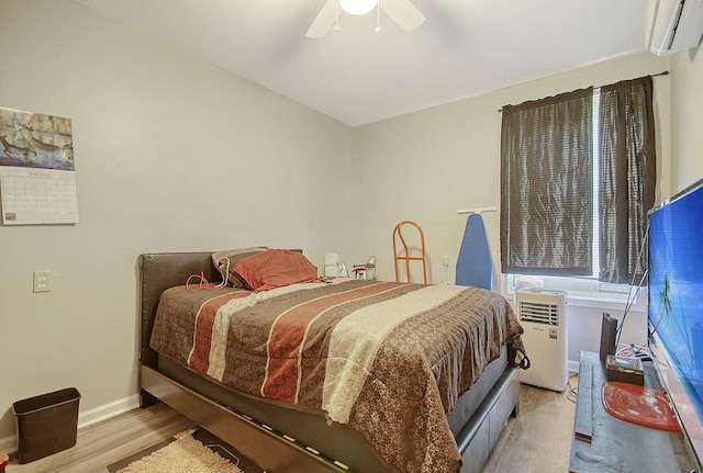 bedroom featuring light hardwood / wood-style flooring, an AC wall unit, and ceiling fan
