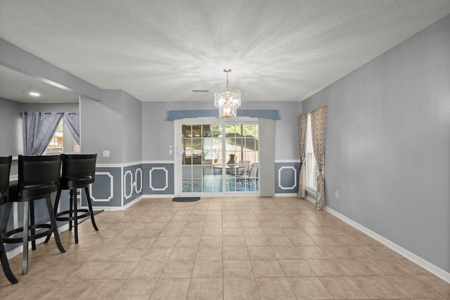 tiled dining space featuring baseboards, an inviting chandelier, and a textured ceiling