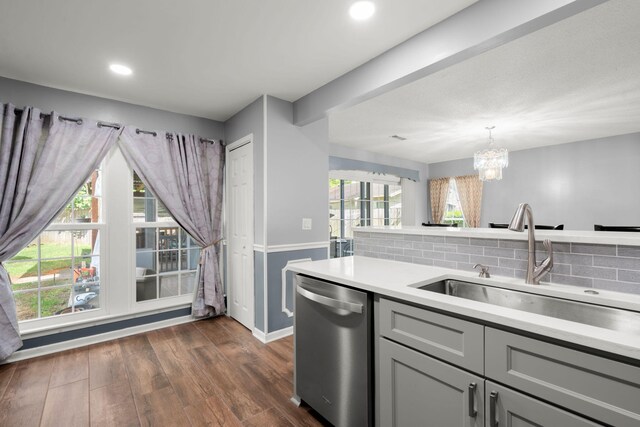 kitchen featuring gray cabinets, light countertops, backsplash, stainless steel dishwasher, and a sink
