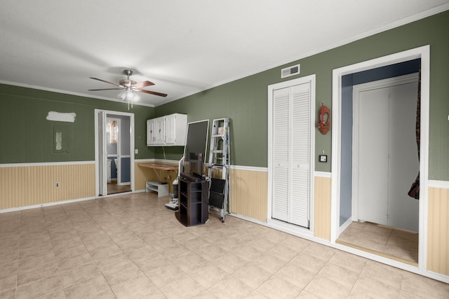 living room with wainscoting, ceiling fan, ornamental molding, and visible vents