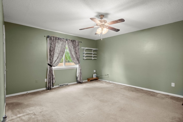carpeted empty room with visible vents, ceiling fan, baseboards, and a textured ceiling