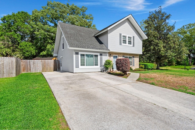 traditional-style house with concrete driveway, a front yard, roof with shingles, and fence