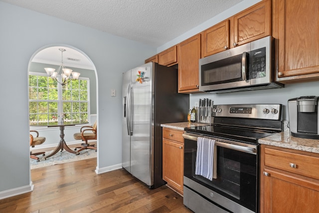 340 Stefan Dr, Charleston, SC 29412 - kitchen with stainless steel appliances, brown cabinets, dark wood-style flooring, a chandelier, and light stone counters