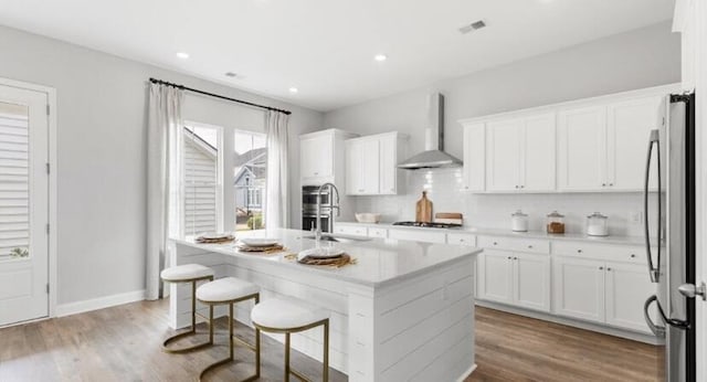 kitchen with freestanding refrigerator, wood finished floors, wall chimney exhaust hood, white cabinets, and a sink