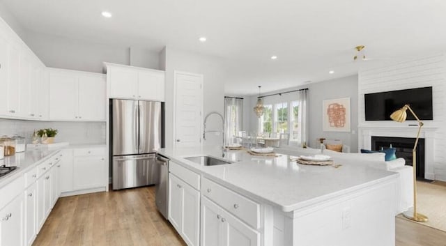 kitchen featuring appliances with stainless steel finishes, a sink, light countertops, an island with sink, and open floor plan