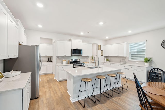 kitchen featuring sink, white cabinetry, appliances with stainless steel finishes, a kitchen island with sink, and light hardwood / wood-style floors