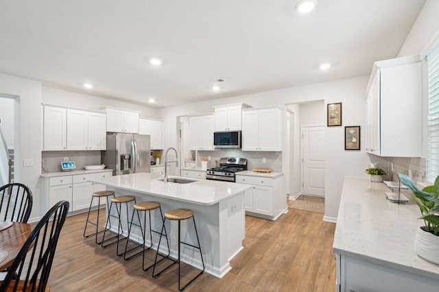 kitchen with white cabinetry, sink, a kitchen breakfast bar, stainless steel appliances, and light hardwood / wood-style flooring