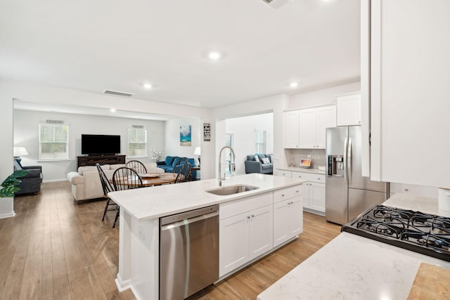 kitchen featuring sink, white cabinetry, light hardwood / wood-style flooring, appliances with stainless steel finishes, and an island with sink