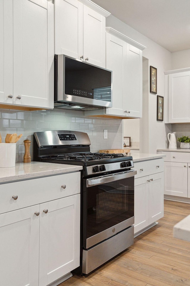 kitchen featuring backsplash, light hardwood / wood-style flooring, white cabinets, and appliances with stainless steel finishes