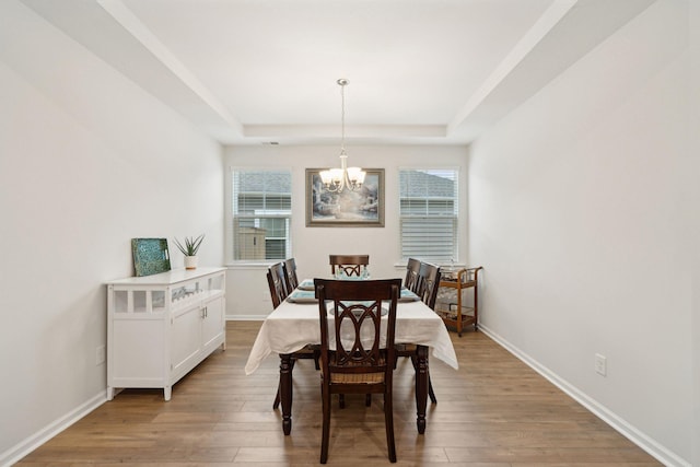 dining space featuring a notable chandelier, a raised ceiling, and light wood-type flooring