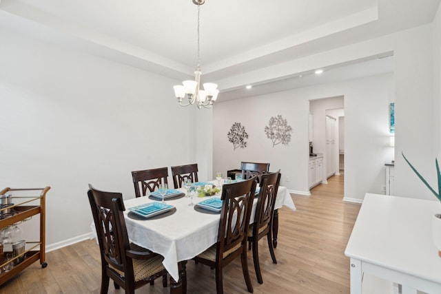 dining space with a chandelier, a raised ceiling, and light hardwood / wood-style flooring