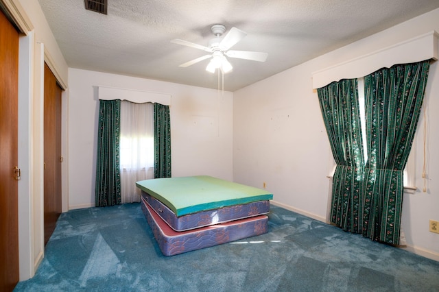 bedroom with dark colored carpet, ceiling fan, a textured ceiling, and a closet