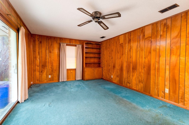 interior space with wooden walls, ceiling fan, and light colored carpet