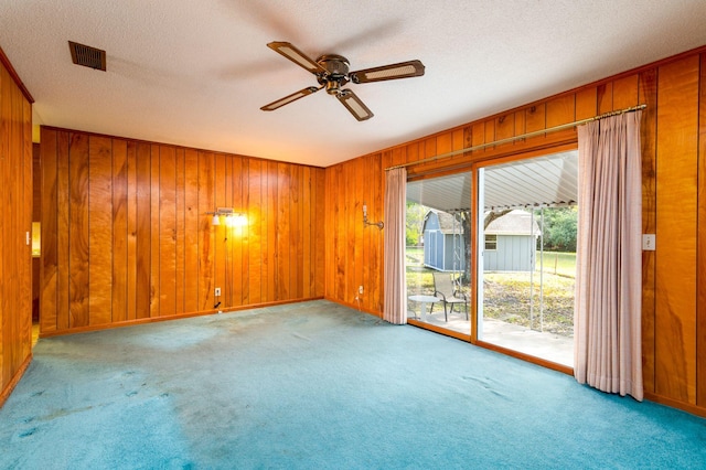 spare room with a textured ceiling, ceiling fan, light carpet, and wooden walls