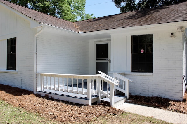 view of exterior entry featuring brick siding and roof with shingles
