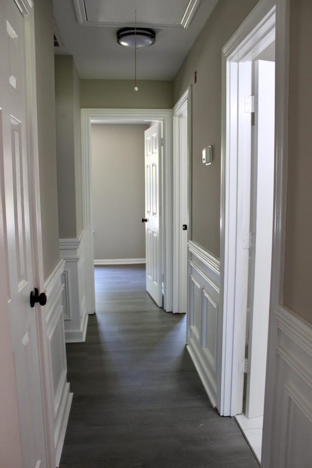hall featuring attic access, dark wood finished floors, a wainscoted wall, and a decorative wall