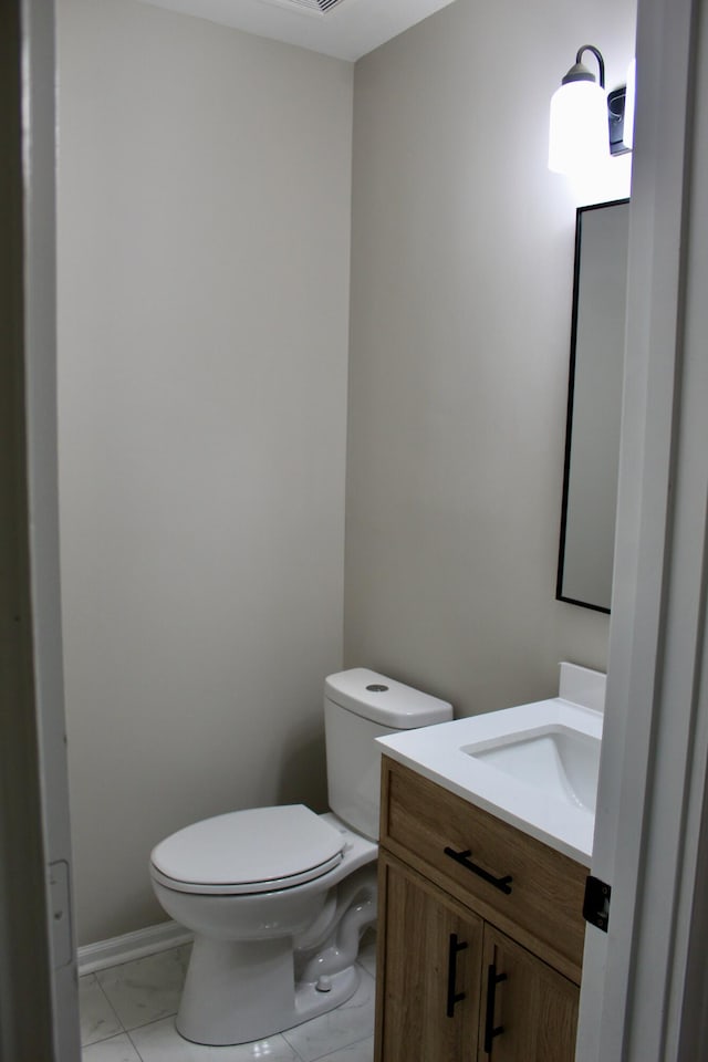 bathroom featuring toilet, vanity, and marble look tile flooring