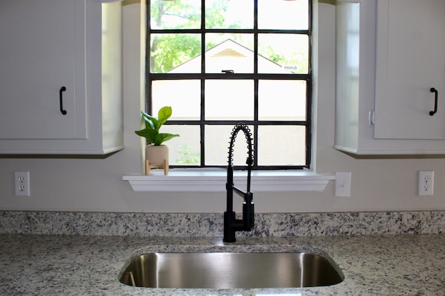 kitchen view of a sink, white cabinetry, and light stone counters