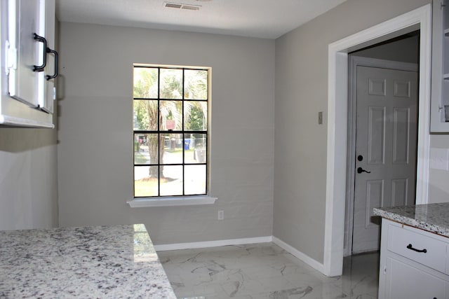 unfurnished dining area featuring light marble finish flooring and baseboards