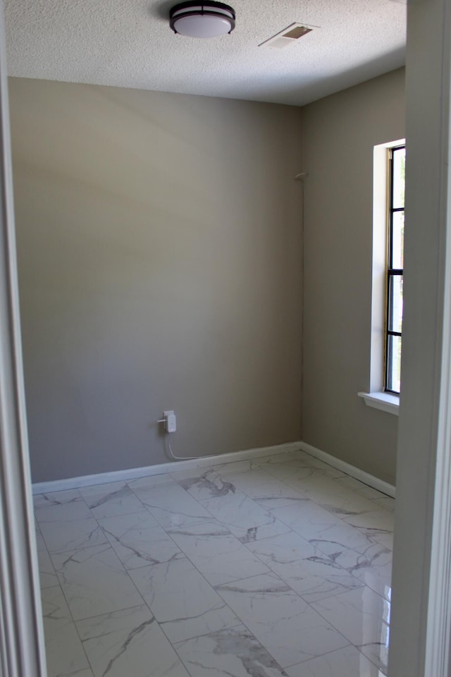 unfurnished room with baseboards, a textured ceiling, plenty of natural light, and light marble finish flooring
