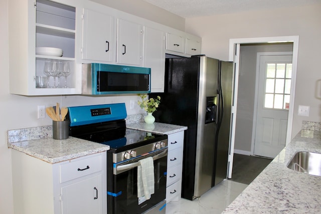kitchen with appliances with stainless steel finishes, open shelves, white cabinetry, light stone countertops, and light marble finish flooring