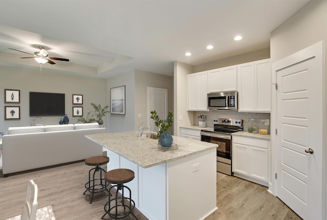 kitchen with a center island with sink, decorative backsplash, light stone countertops, white cabinetry, and stainless steel appliances