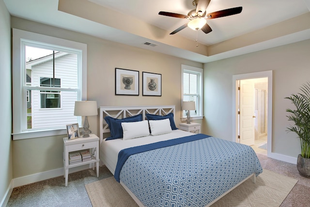 bedroom featuring a raised ceiling, ceiling fan, light colored carpet, and ensuite bathroom