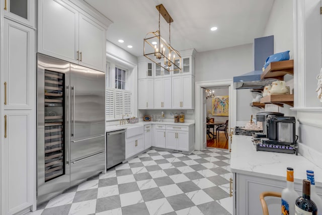 kitchen featuring appliances with stainless steel finishes, pendant lighting, white cabinets, a notable chandelier, and wall chimney exhaust hood