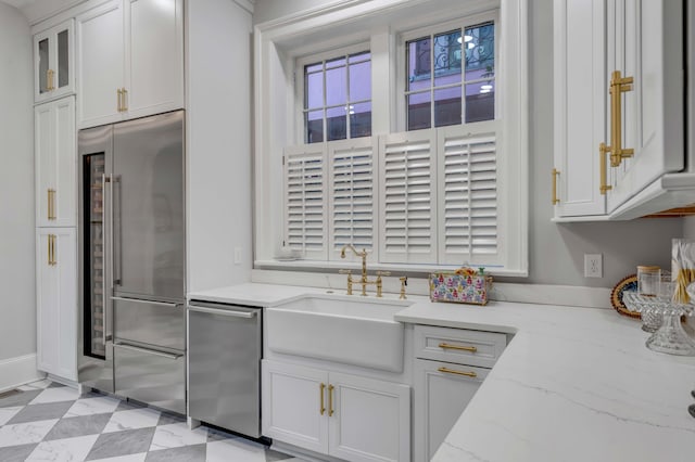 kitchen with white cabinetry, stainless steel appliances, light stone countertops, and sink