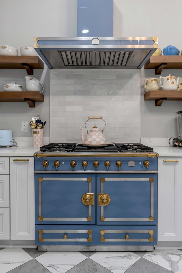 kitchen with white cabinetry, decorative backsplash, range with two ovens, light stone counters, and wall chimney exhaust hood