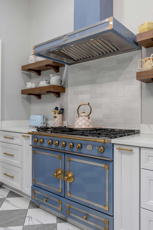 kitchen featuring tasteful backsplash, white cabinets, island exhaust hood, range, and light stone countertops