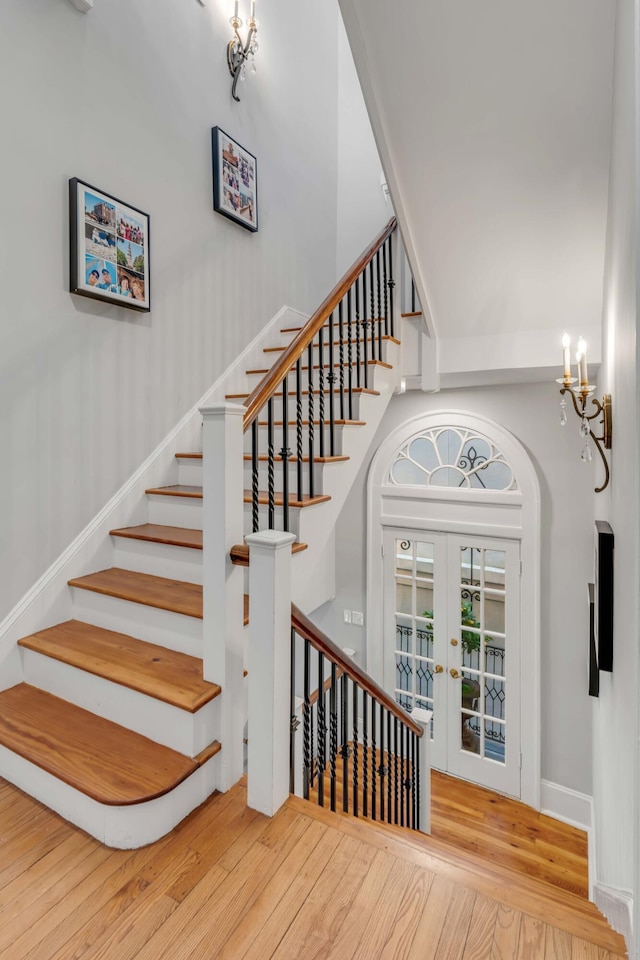 staircase with hardwood / wood-style flooring, an inviting chandelier, and french doors