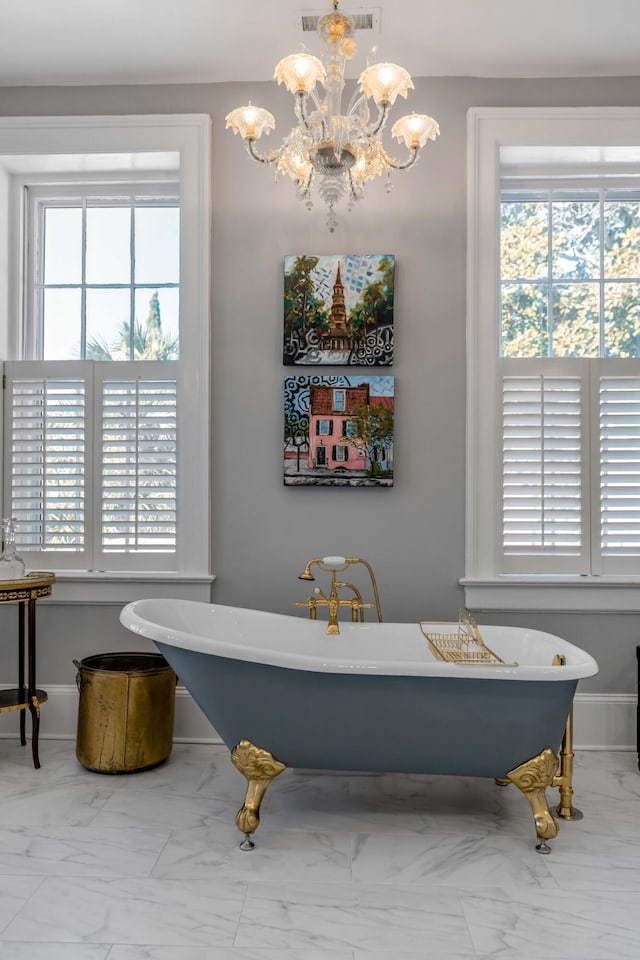 bathroom with a healthy amount of sunlight, a notable chandelier, and a bathtub