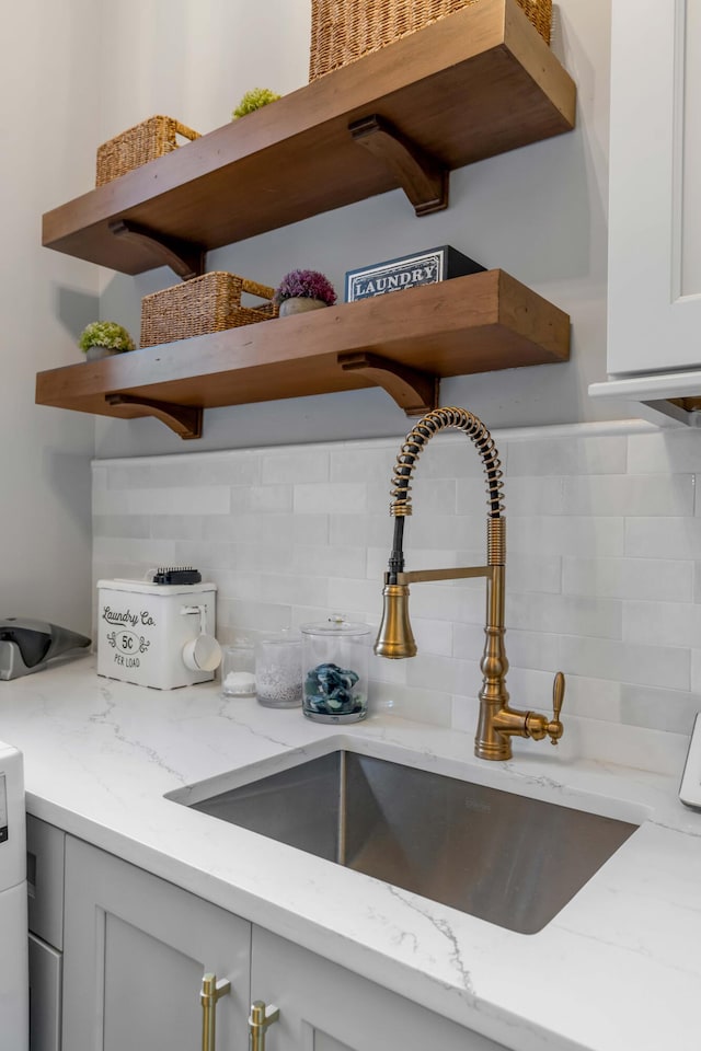 room details with tasteful backsplash, light stone countertops, sink, and white cabinets