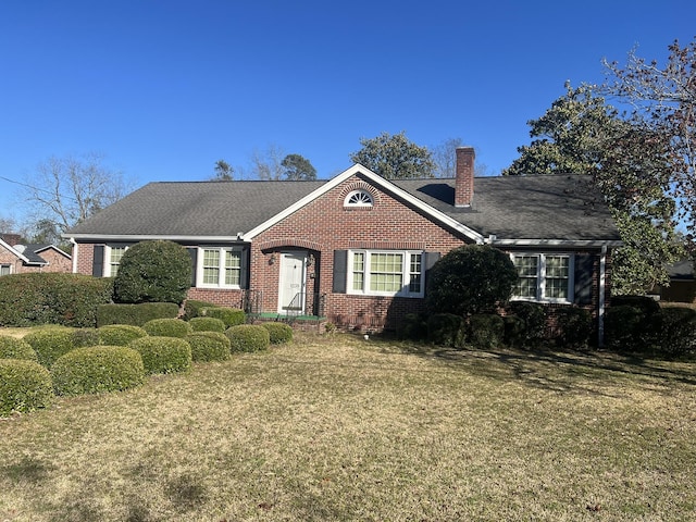 ranch-style house featuring brick siding, a chimney, a front yard, and a shingled roof