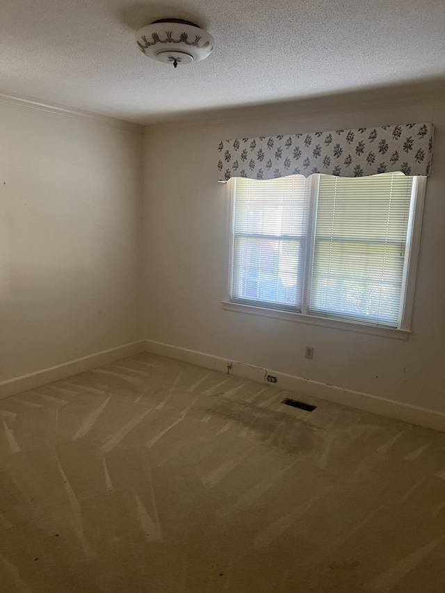 spare room featuring baseboards, light colored carpet, visible vents, and a textured ceiling