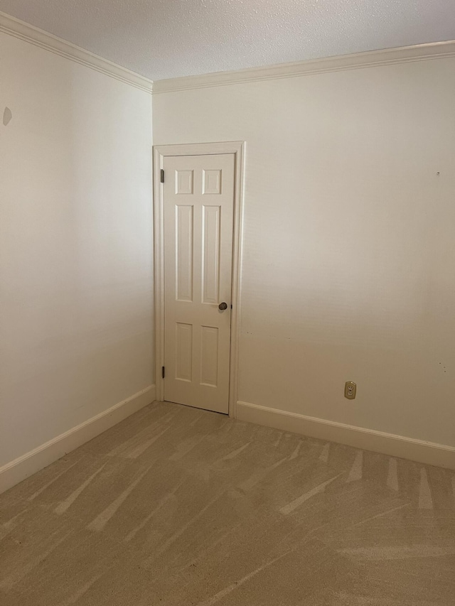 empty room featuring a textured ceiling, ornamental molding, baseboards, and light colored carpet