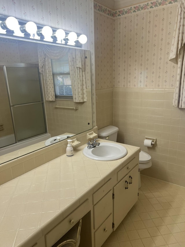 full bath featuring wallpapered walls, toilet, a wainscoted wall, tile patterned floors, and tile walls