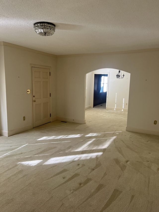 empty room with arched walkways, ornamental molding, a textured ceiling, and light carpet