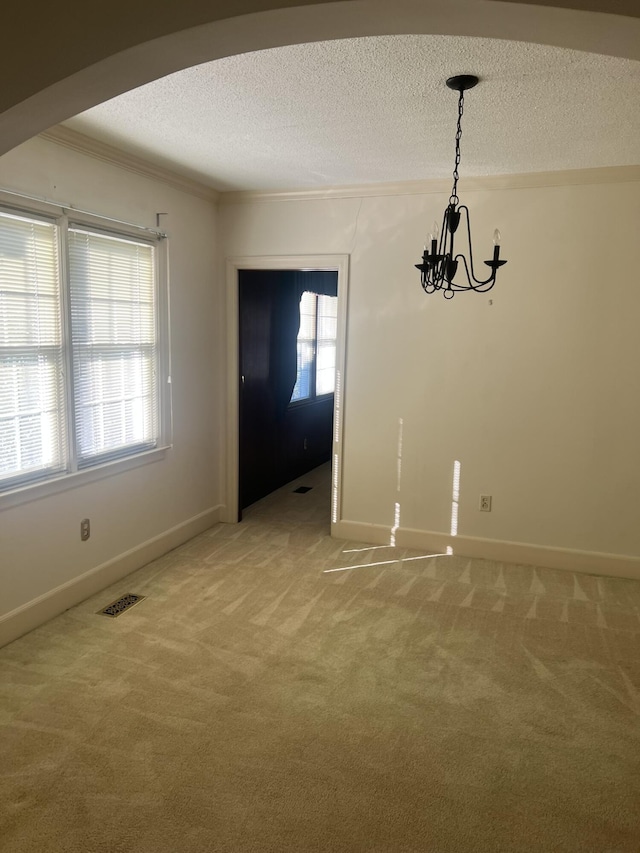 unfurnished dining area with arched walkways, light colored carpet, visible vents, ornamental molding, and a textured ceiling