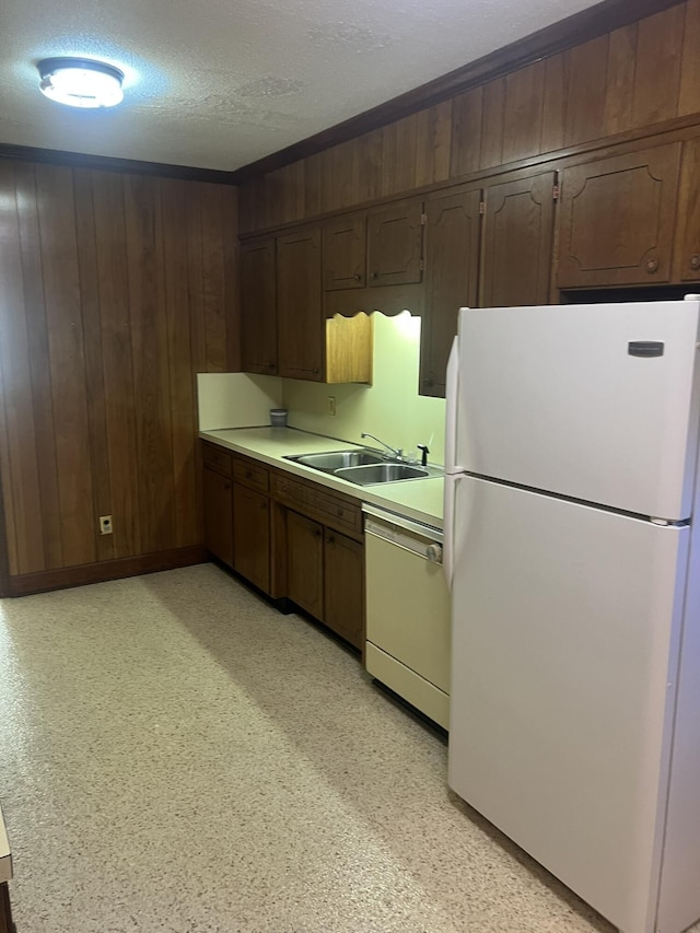 kitchen with white appliances, light countertops, a textured ceiling, wood walls, and a sink