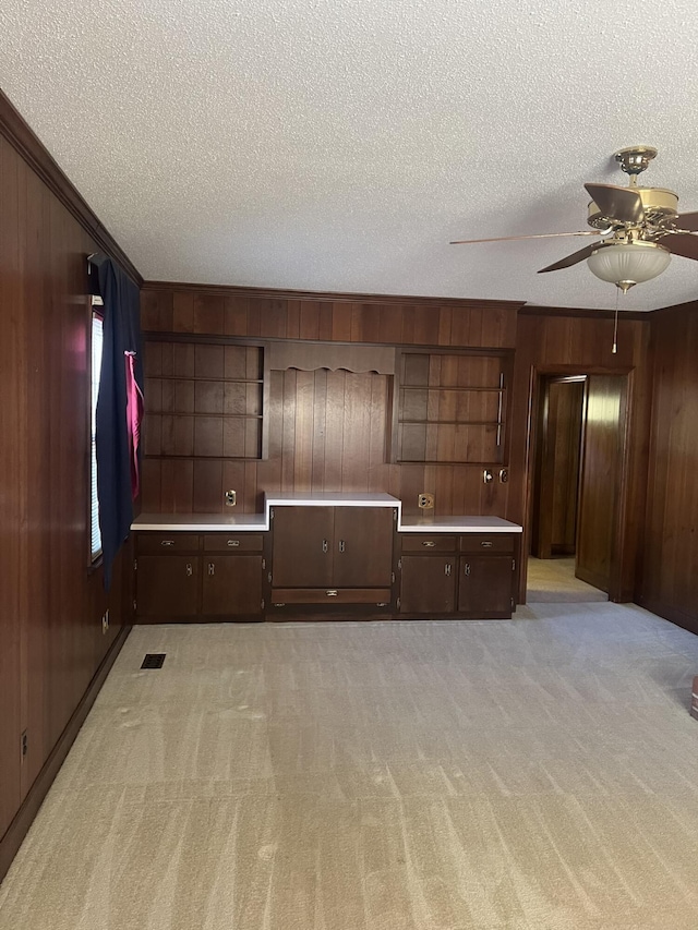 interior space with a textured ceiling, ceiling fan, wooden walls, light colored carpet, and crown molding