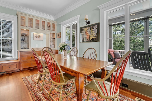 dining space with ornamental molding and light hardwood / wood-style floors