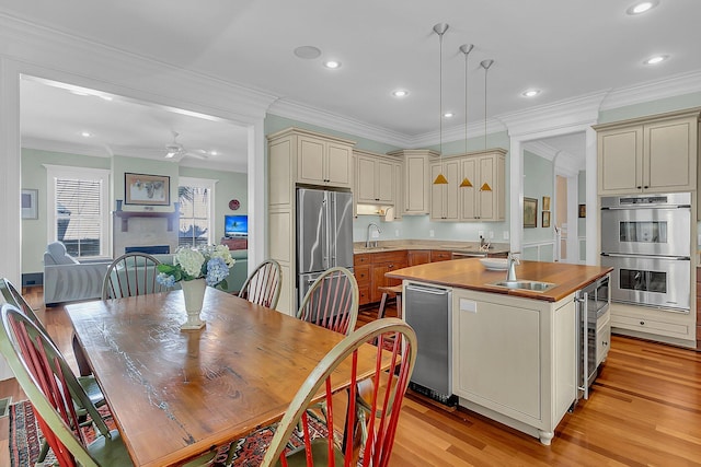 dining room with ceiling fan, sink, light wood-type flooring, and ornamental molding