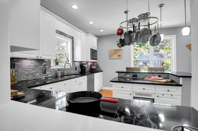 kitchen with white cabinetry, a sink, light wood finished floors, backsplash, and stainless steel appliances